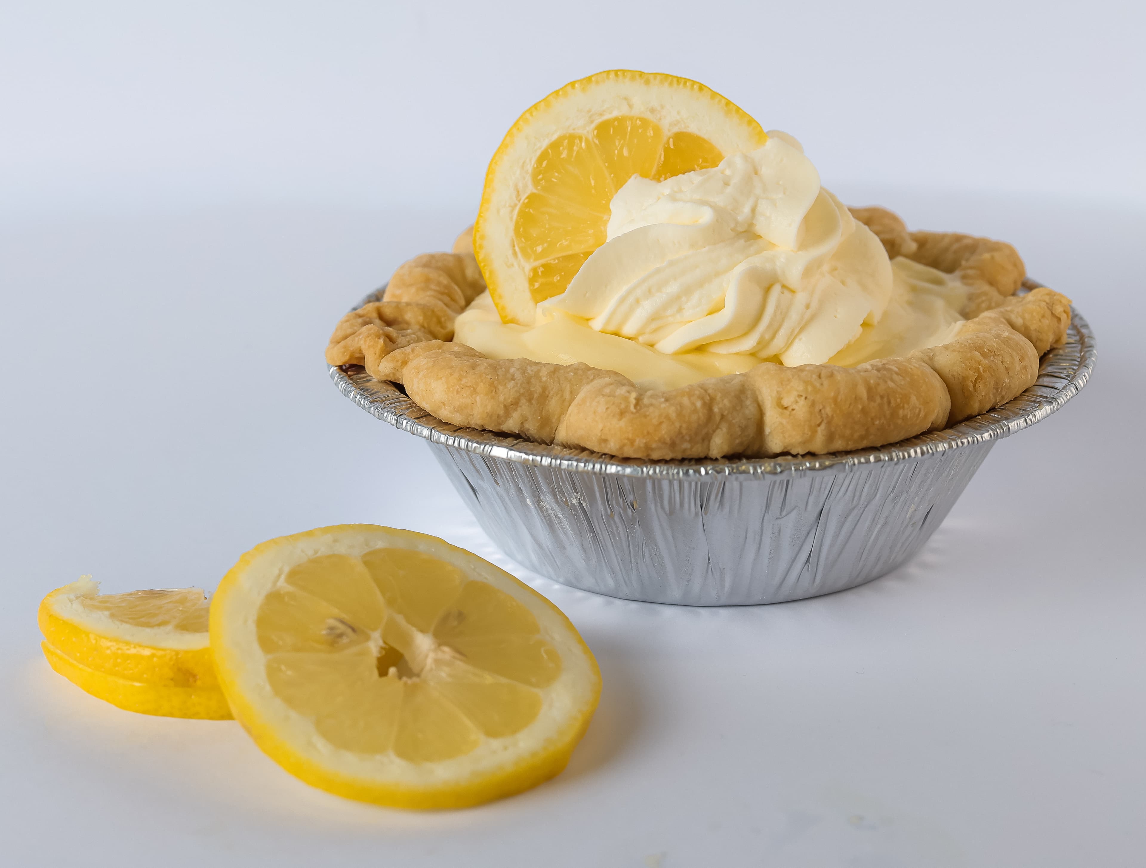 Small lemon tart in a foil tin with whipped cream and fresh lemon slices.
