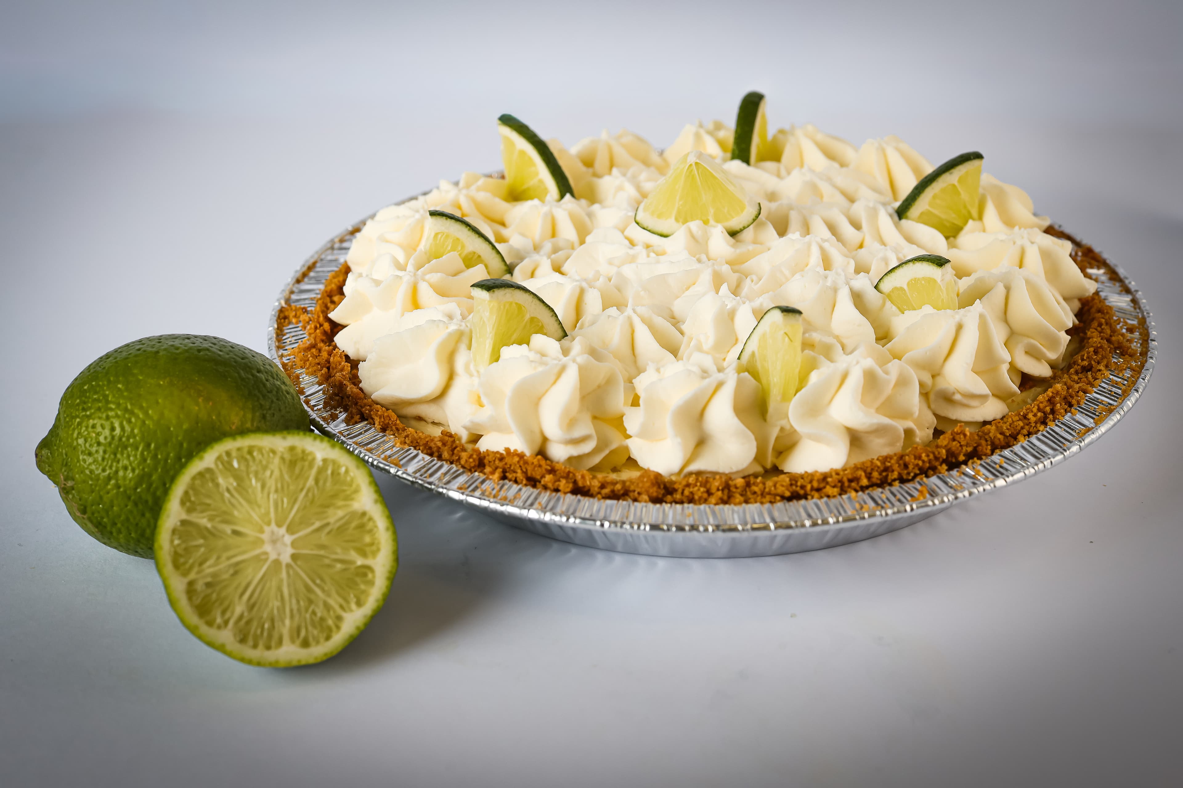 Key lime pie topped with whipped cream swirls and lime wedges beside fresh limes.
