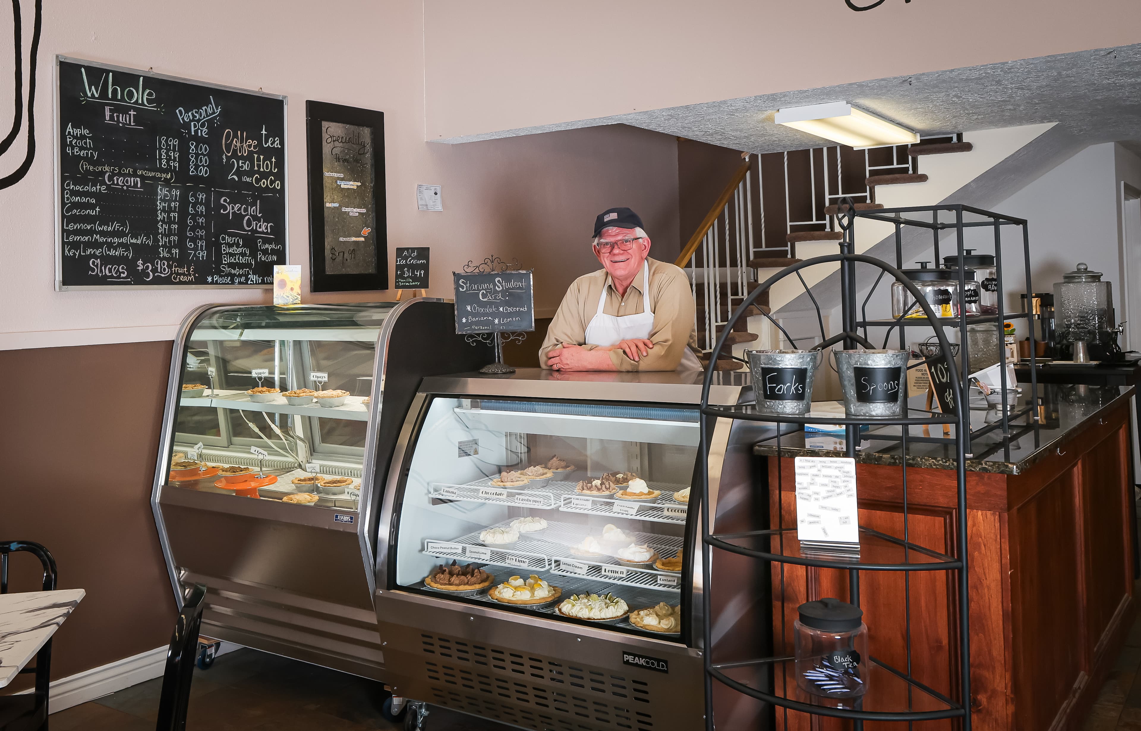 Smiling man in an apron stands behind glass display cases filled with assorted fresh pies.