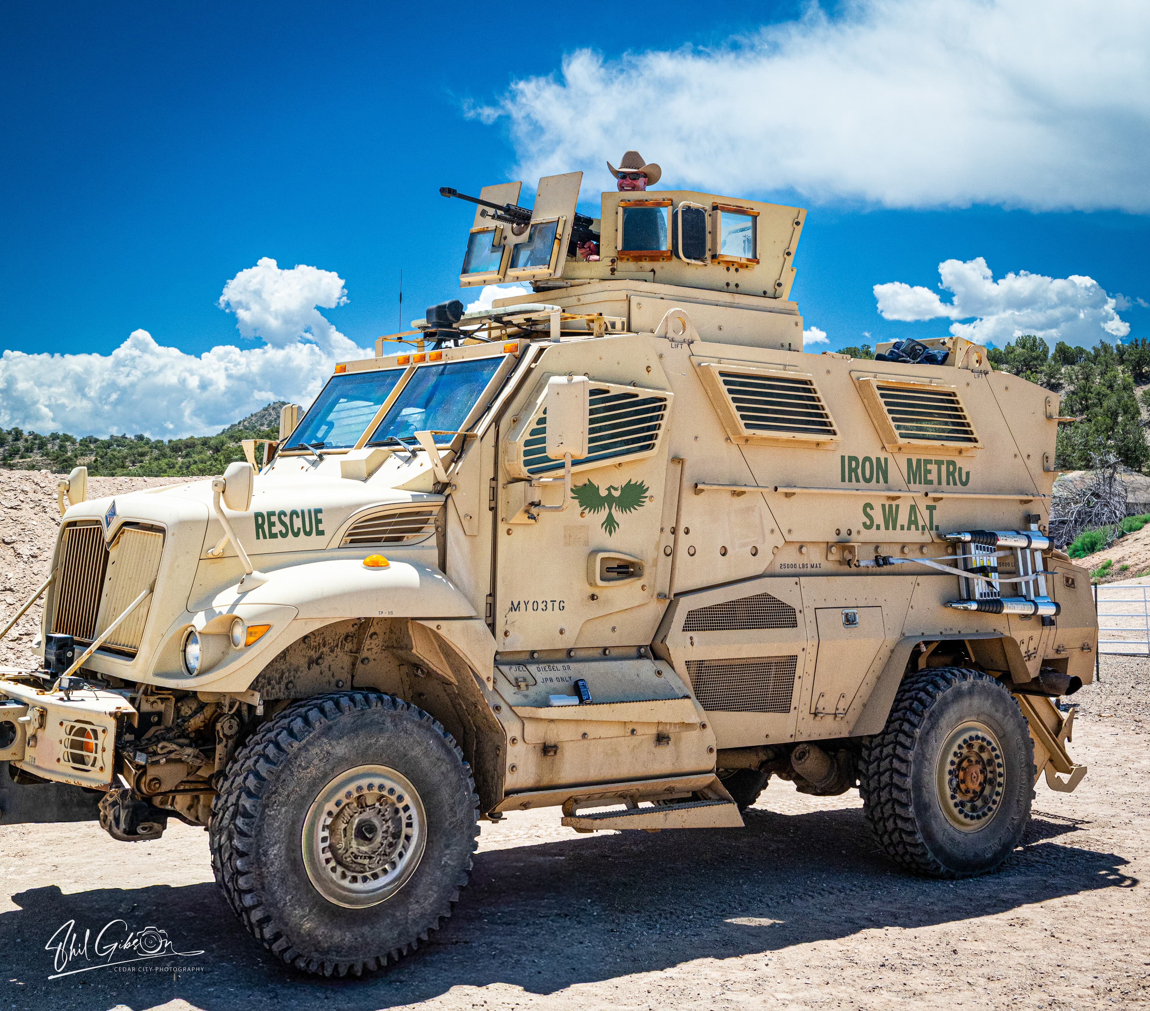 Tan armored SWAT rescue vehicle with a man in a cowboy hat in the turret.