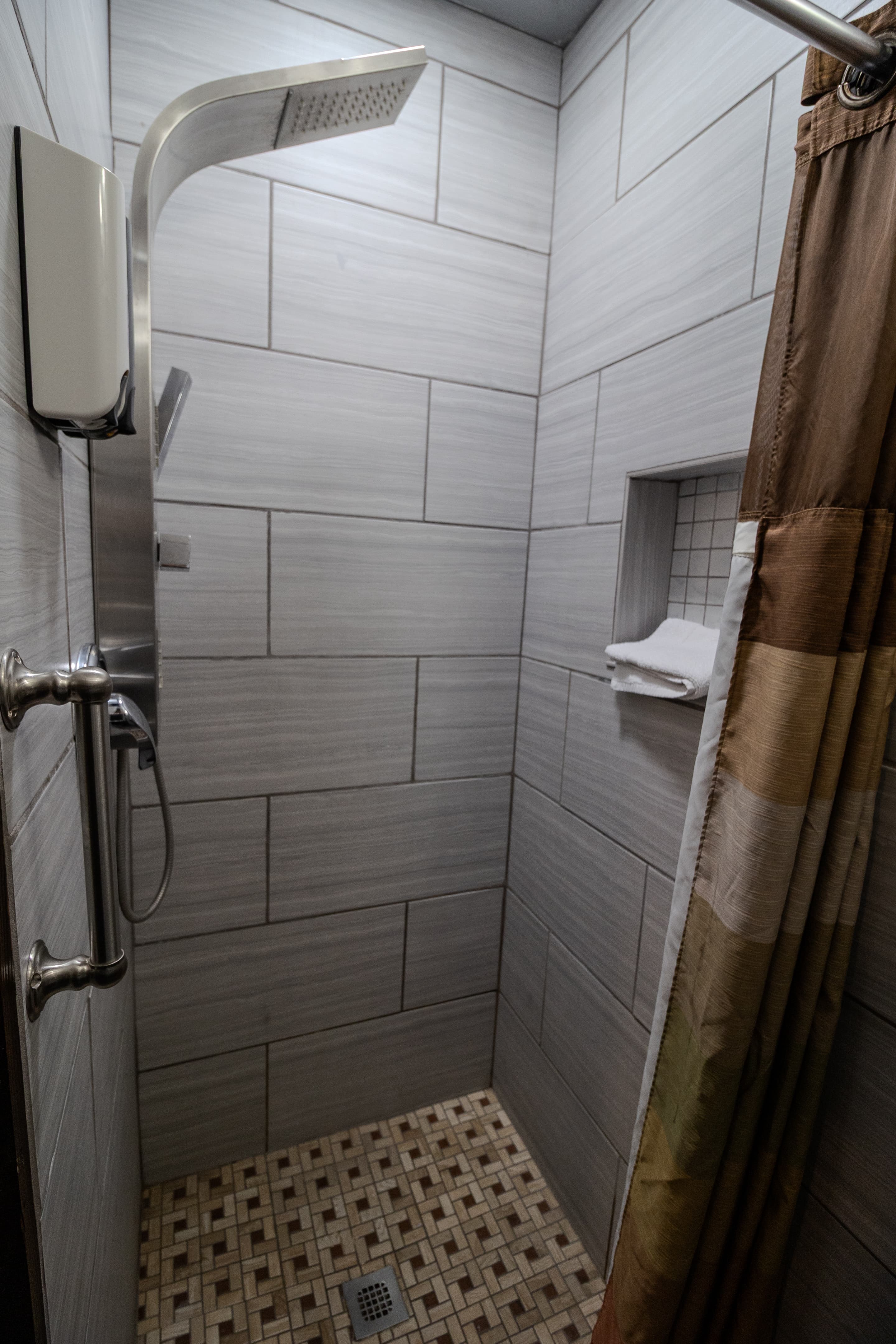 Modern grey tiled shower with a rainfall showerhead, grab bar, and brown striped curtain.