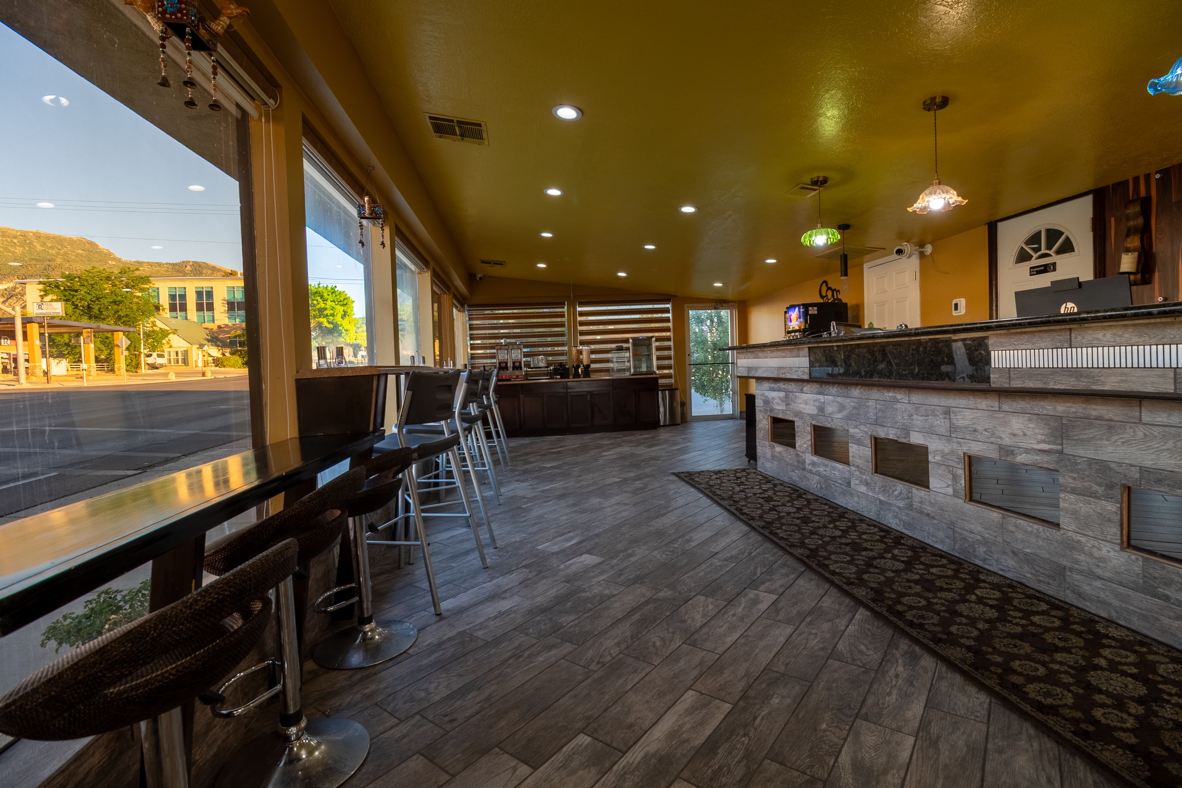 Modern cafe interior with window seating overlooking a street, stone counter, and yellow ceiling.