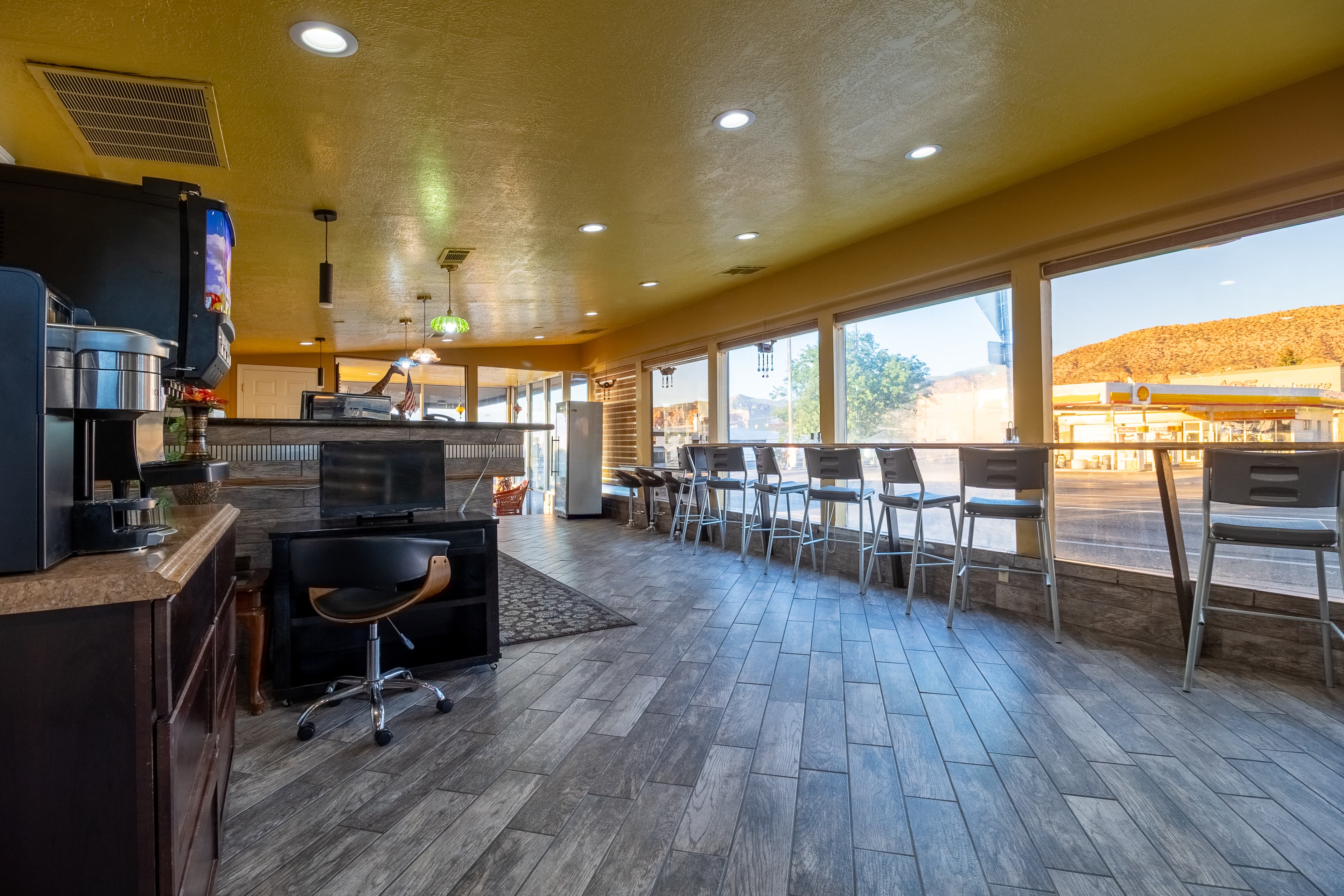 Cafe interior with window seating, stools, and a coffee station overlooking a desert landscape.