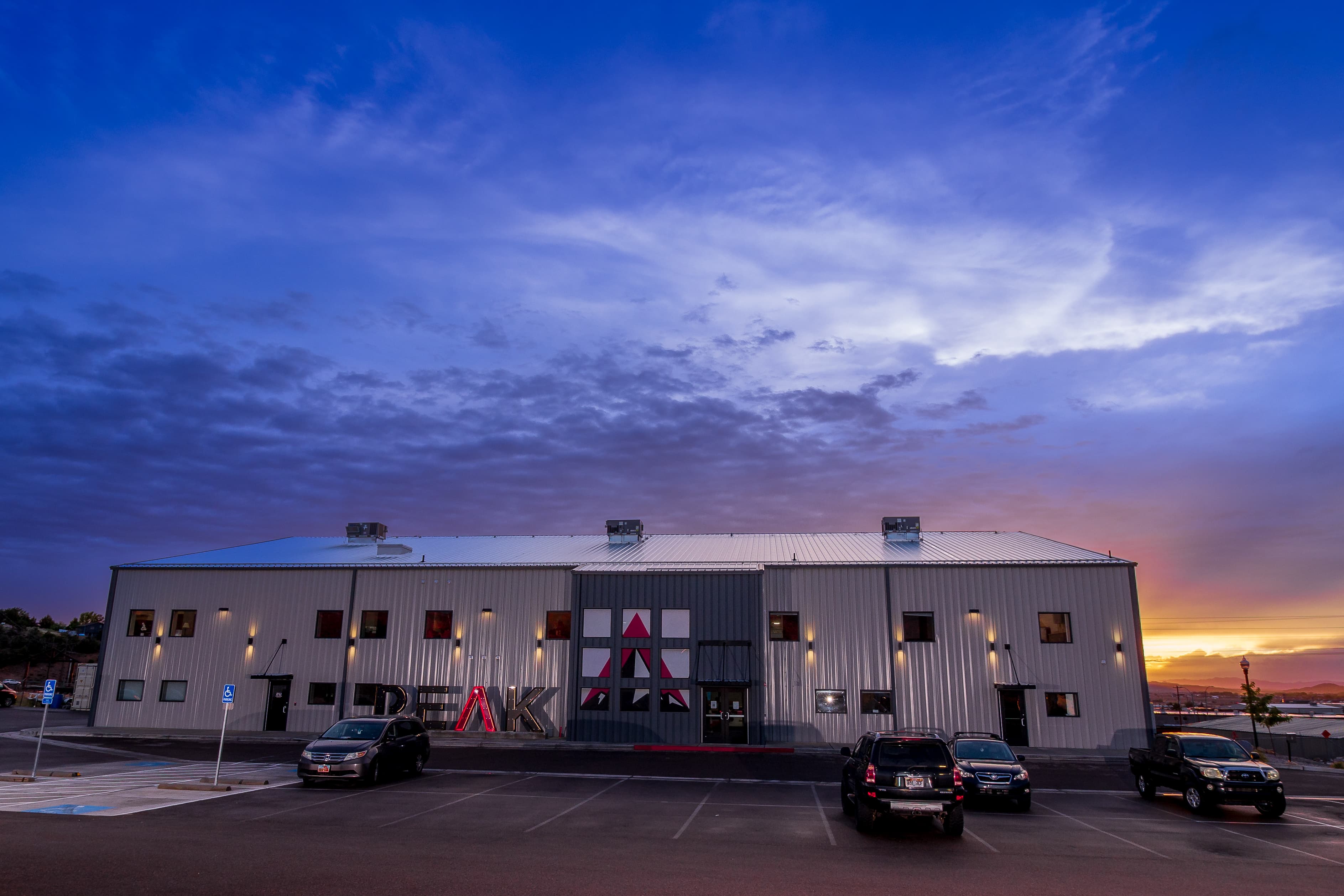 Modern industrial building with "PEAK" signage and mountain logo under a vibrant sunset sky.